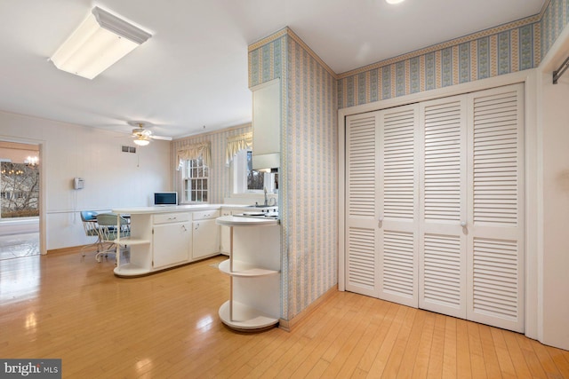 kitchen with sink, light wood-type flooring, kitchen peninsula, ceiling fan, and white cabinets