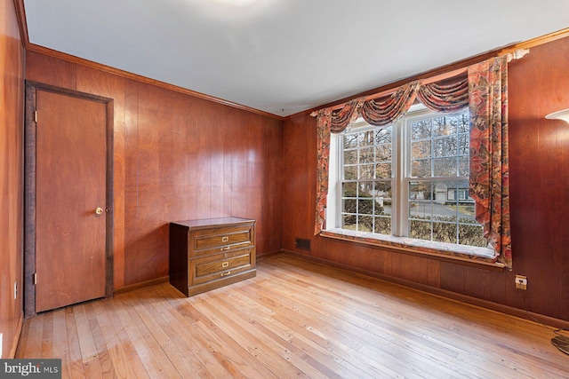 unfurnished room featuring ornamental molding, wooden walls, and light wood-type flooring