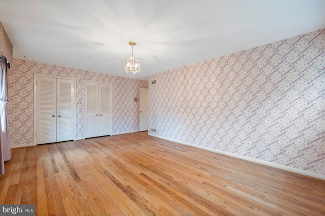 unfurnished bedroom featuring multiple closets, a chandelier, and light wood-type flooring