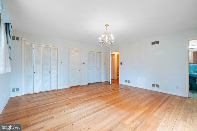 unfurnished bedroom featuring multiple closets, an inviting chandelier, light wood-type flooring, and ensuite bath