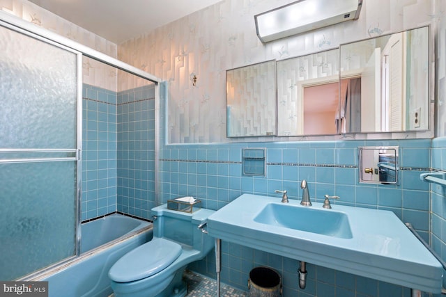 full bathroom with toilet, bath / shower combo with glass door, sink, and tile walls