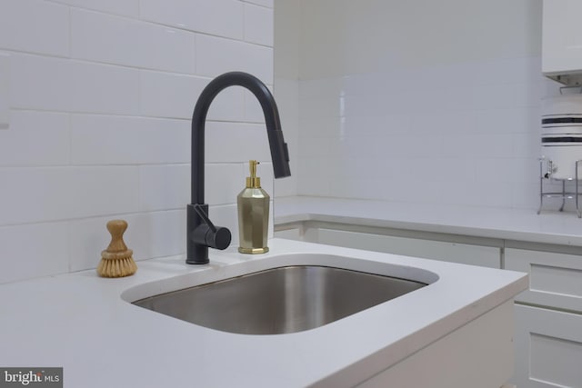 interior details with backsplash, sink, water heater, and white cabinets