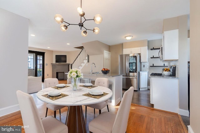 dining space featuring a brick fireplace, hardwood / wood-style flooring, a notable chandelier, and sink