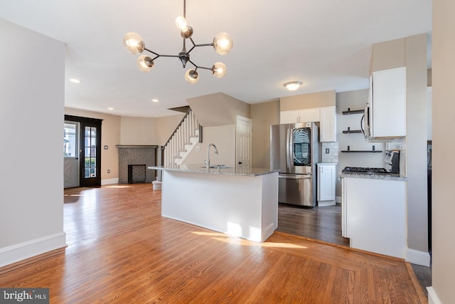 kitchen with white cabinetry, a brick fireplace, light hardwood / wood-style flooring, stainless steel refrigerator, and light stone countertops