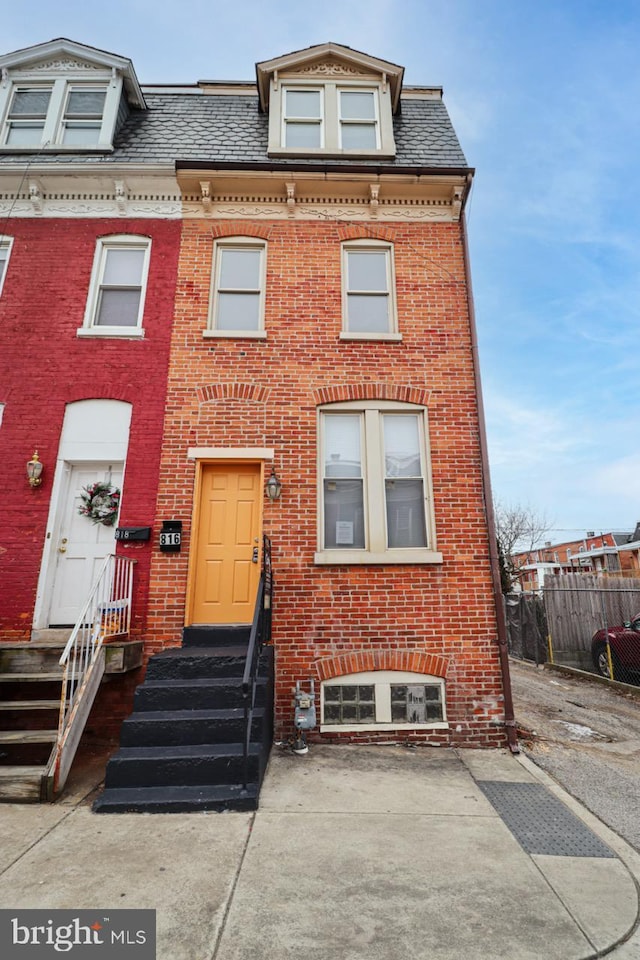 victorian home featuring entry steps, fence, mansard roof, and brick siding