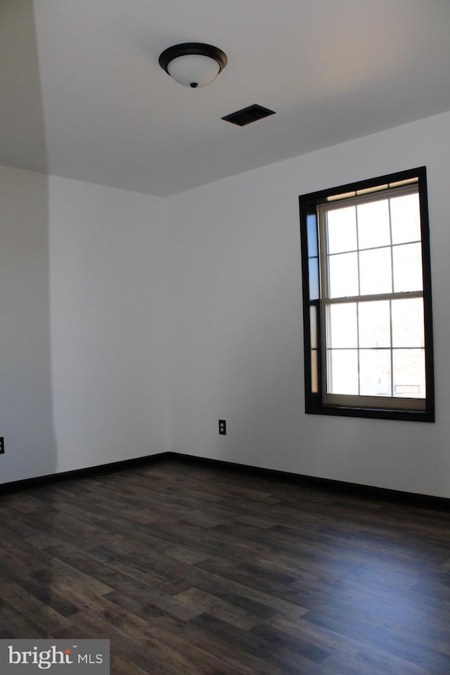 spare room with dark wood-type flooring, a wealth of natural light, and baseboards