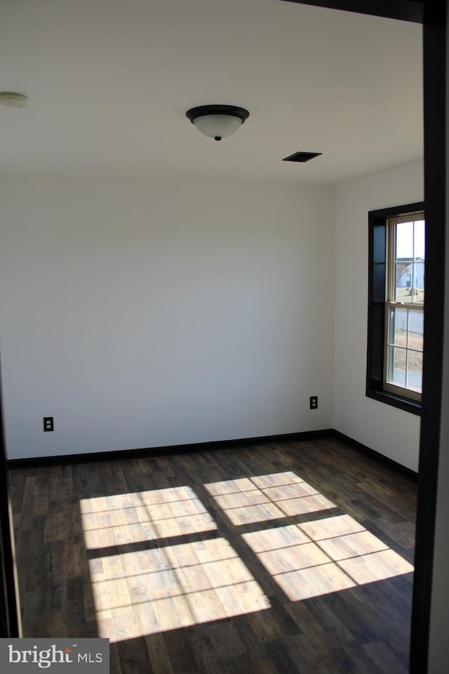 spare room featuring dark wood-style floors, visible vents, and baseboards