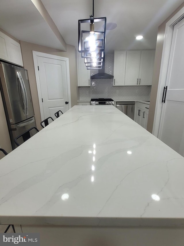 kitchen featuring pendant lighting, white cabinetry, decorative backsplash, light stone counters, and stainless steel appliances