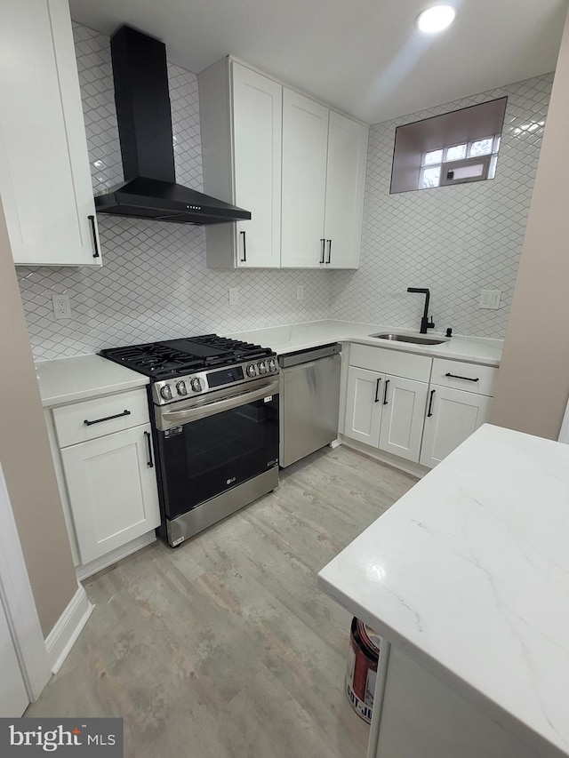 kitchen featuring wall chimney range hood, sink, light hardwood / wood-style flooring, appliances with stainless steel finishes, and white cabinets