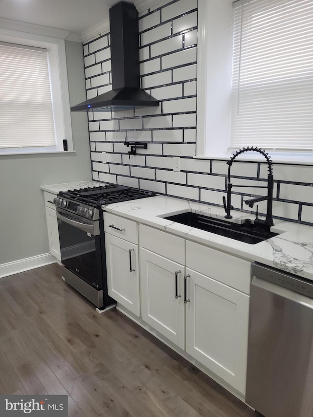 kitchen with sink, wall chimney range hood, stainless steel appliances, light stone countertops, and white cabinets