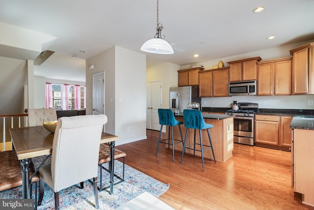 kitchen featuring a kitchen bar, decorative light fixtures, a center island, light wood-type flooring, and appliances with stainless steel finishes