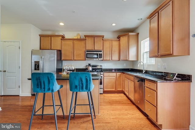 kitchen with sink, appliances with stainless steel finishes, dark stone countertops, a kitchen island, and light wood-type flooring