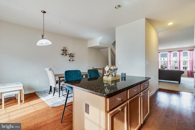 kitchen with a kitchen island, a breakfast bar, pendant lighting, dark stone counters, and hardwood / wood-style flooring