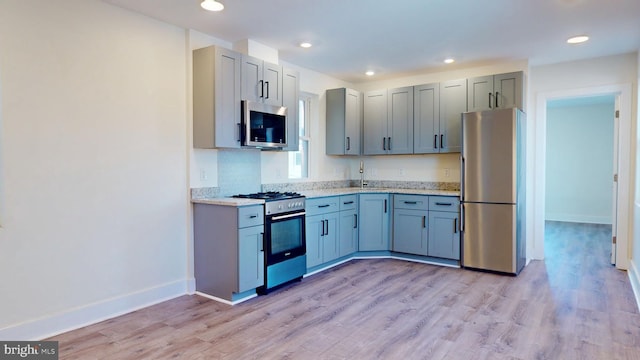 kitchen featuring light wood finished floors, appliances with stainless steel finishes, a sink, and baseboards