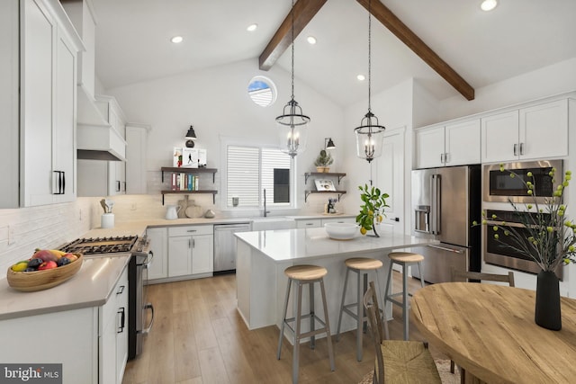 kitchen with beam ceiling, stainless steel appliances, white cabinets, a kitchen island, and decorative light fixtures