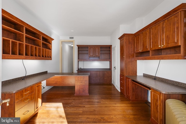 unfurnished office featuring dark hardwood / wood-style flooring, radiator heating unit, and built in desk