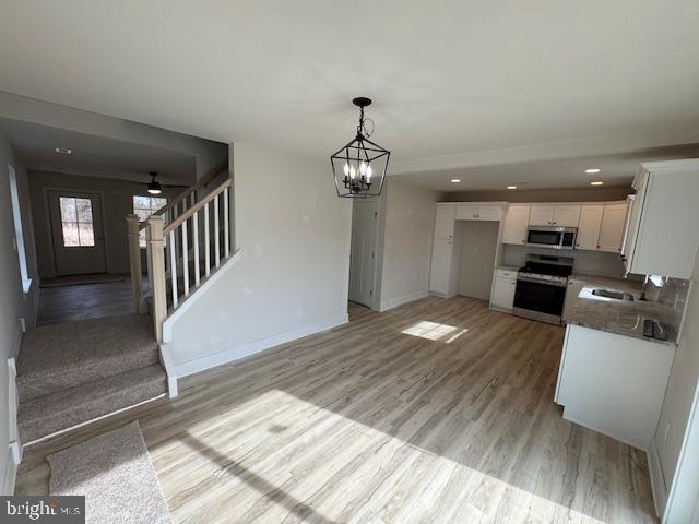 kitchen with baseboards, white cabinets, appliances with stainless steel finishes, open floor plan, and light wood-style floors