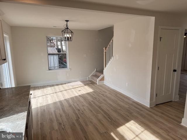 unfurnished dining area with an inviting chandelier, baseboards, stairway, and wood finished floors