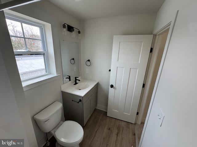 half bath with toilet, wood finished floors, and vanity