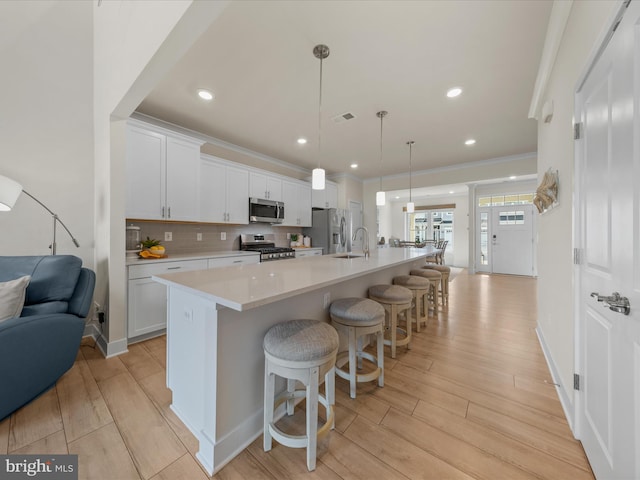 kitchen with a breakfast bar area, white cabinetry, hanging light fixtures, a large island with sink, and appliances with stainless steel finishes