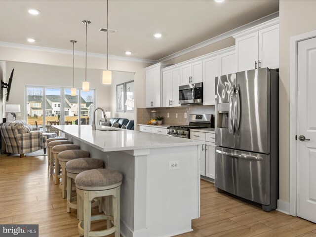 kitchen with appliances with stainless steel finishes, a breakfast bar, an island with sink, sink, and hanging light fixtures
