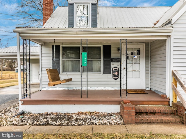 entrance to property featuring a porch, metal roof, and a chimney