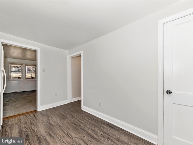 unfurnished room featuring baseboards and dark wood-type flooring