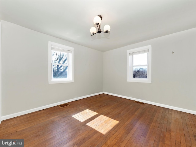 empty room with a notable chandelier, wood-type flooring, visible vents, and baseboards