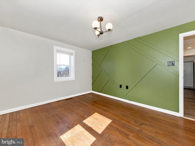 empty room with baseboards, visible vents, and hardwood / wood-style floors