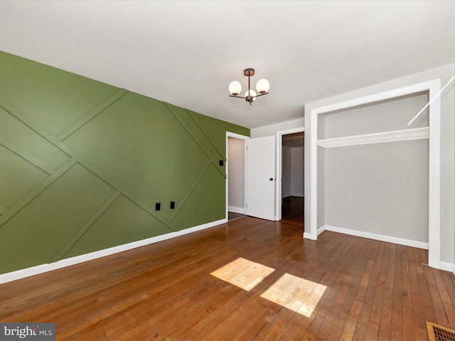 unfurnished bedroom with baseboards, dark wood-style flooring, visible vents, and an inviting chandelier