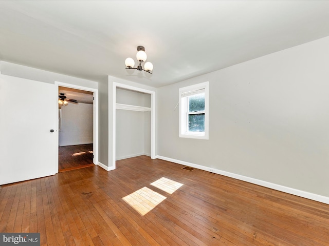 unfurnished bedroom featuring a closet, a notable chandelier, dark wood finished floors, and baseboards