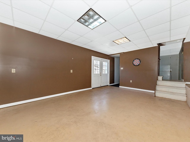 empty room with baseboards, a drop ceiling, stairs, finished concrete floors, and french doors