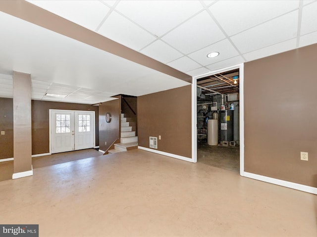 basement featuring a paneled ceiling, water heater, stairway, and baseboards