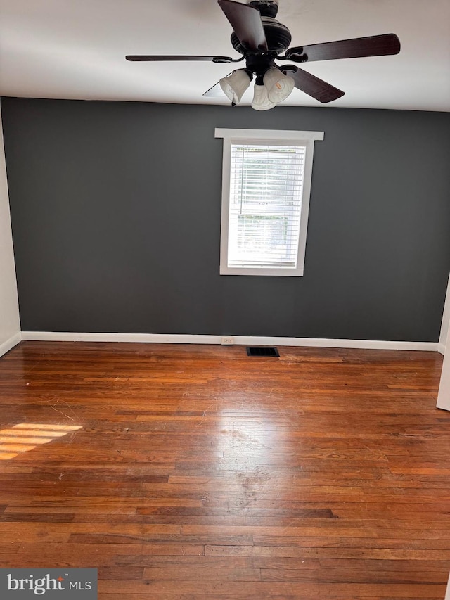 unfurnished room featuring dark wood-type flooring, a ceiling fan, visible vents, and baseboards