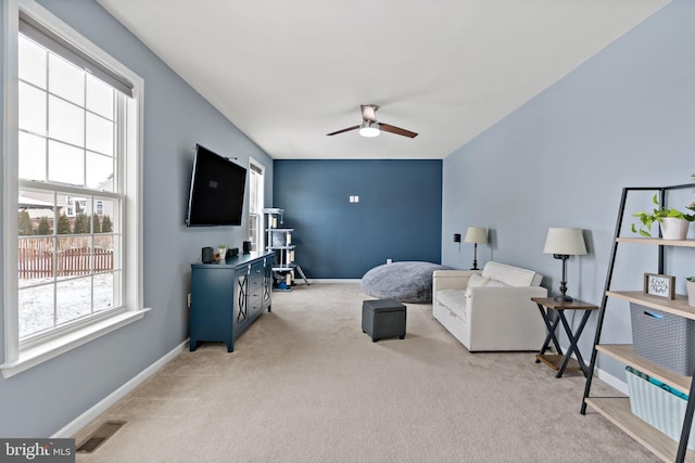 living area featuring baseboards, visible vents, light carpet, and ceiling fan