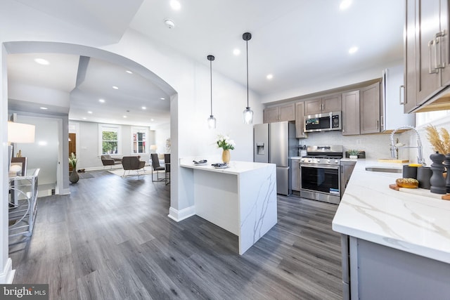 kitchen with pendant lighting, sink, dark wood-type flooring, stainless steel appliances, and light stone countertops