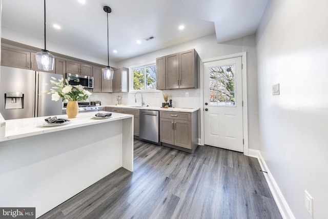 kitchen featuring sink, dark wood-type flooring, backsplash, stainless steel appliances, and decorative light fixtures