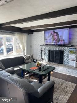 living room featuring beamed ceiling, wood-type flooring, and a brick fireplace