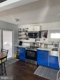 kitchen featuring stainless steel appliances, white cabinetry, blue cabinetry, and dark wood-type flooring