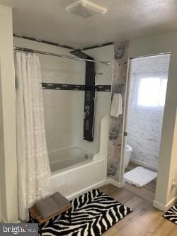 bathroom with shower / bath combo, brick wall, and wood-type flooring