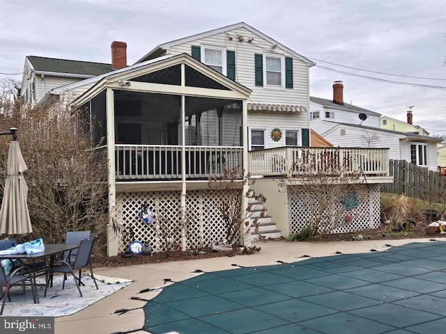 rear view of property with a sunroom, a covered pool, a chimney, stairs, and fence