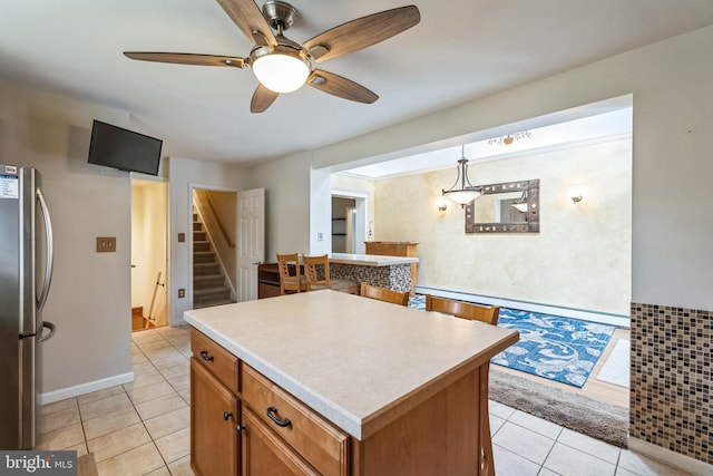 kitchen with hanging light fixtures, light tile patterned floors, stainless steel refrigerator, and a kitchen island