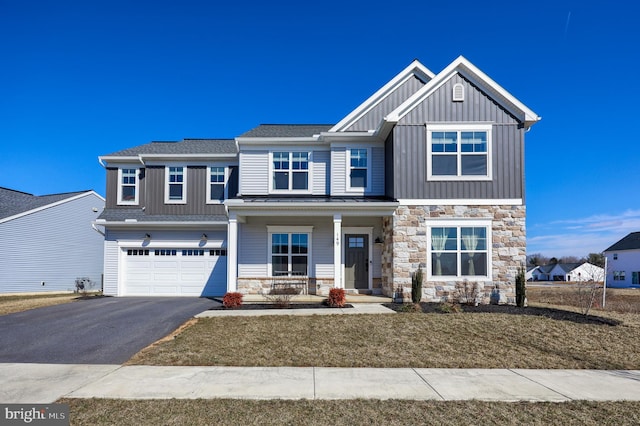 craftsman-style house featuring an attached garage, covered porch, driveway, stone siding, and board and batten siding