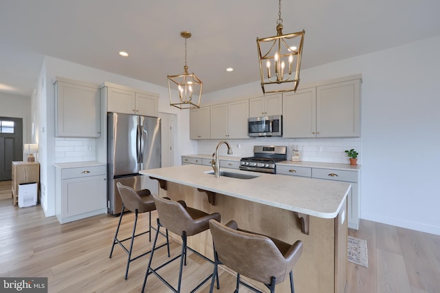 kitchen with appliances with stainless steel finishes, a kitchen breakfast bar, a kitchen island with sink, pendant lighting, and a sink