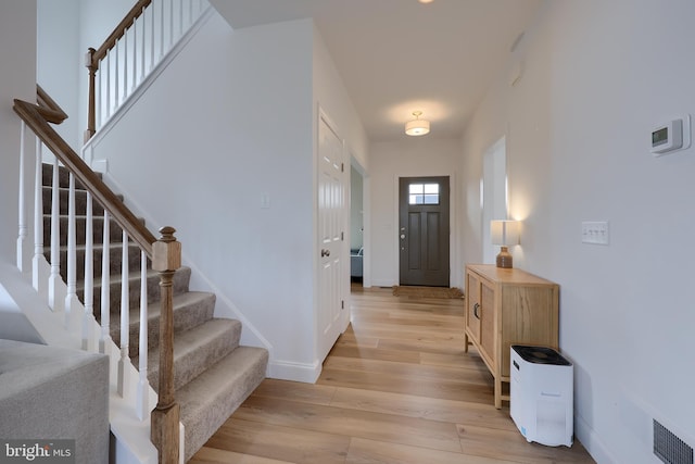 entryway with light wood-style floors, baseboards, stairs, and visible vents