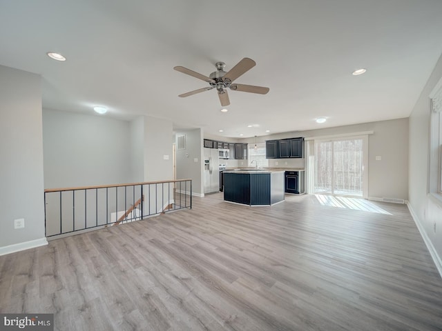 unfurnished living room featuring baseboards, recessed lighting, a sink, and light wood-style floors