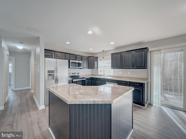 kitchen featuring a kitchen island, hanging light fixtures, appliances with stainless steel finishes, light wood-type flooring, and light stone countertops