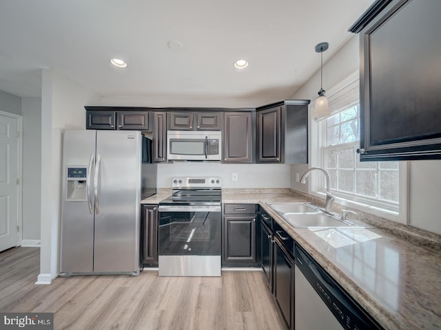 kitchen with appliances with stainless steel finishes, hanging light fixtures, light wood-style floors, a sink, and recessed lighting