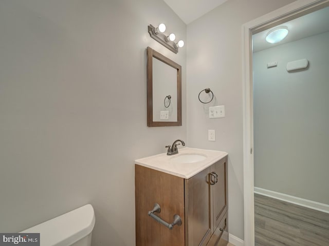 bathroom with toilet, wood finished floors, vanity, and baseboards