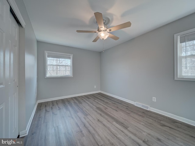 empty room with a ceiling fan, light wood-type flooring, visible vents, and baseboards